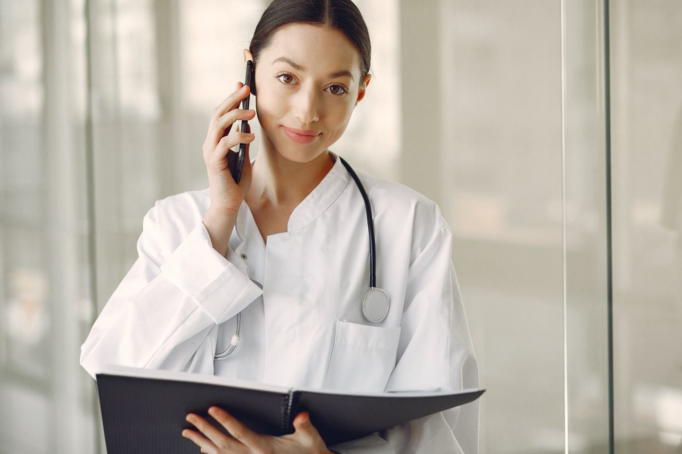 A Medicentres physician in a white coat takes a phone call while reviewing a patient file